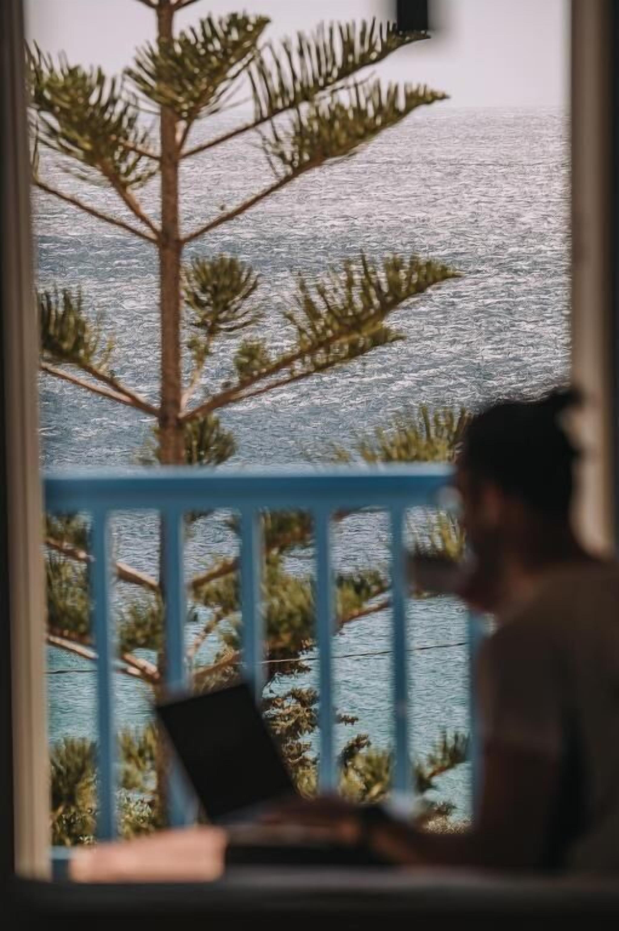 Ein Zimmer mit Meerblick, einem blauen Geländer und einem Laptop auf einem Tisch.