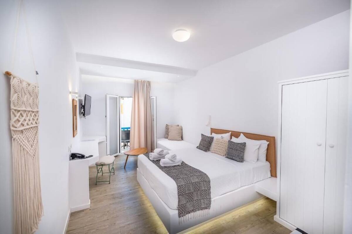 A hotel room with a bed, a small seating area, a wardrobe, and a view of the outside.