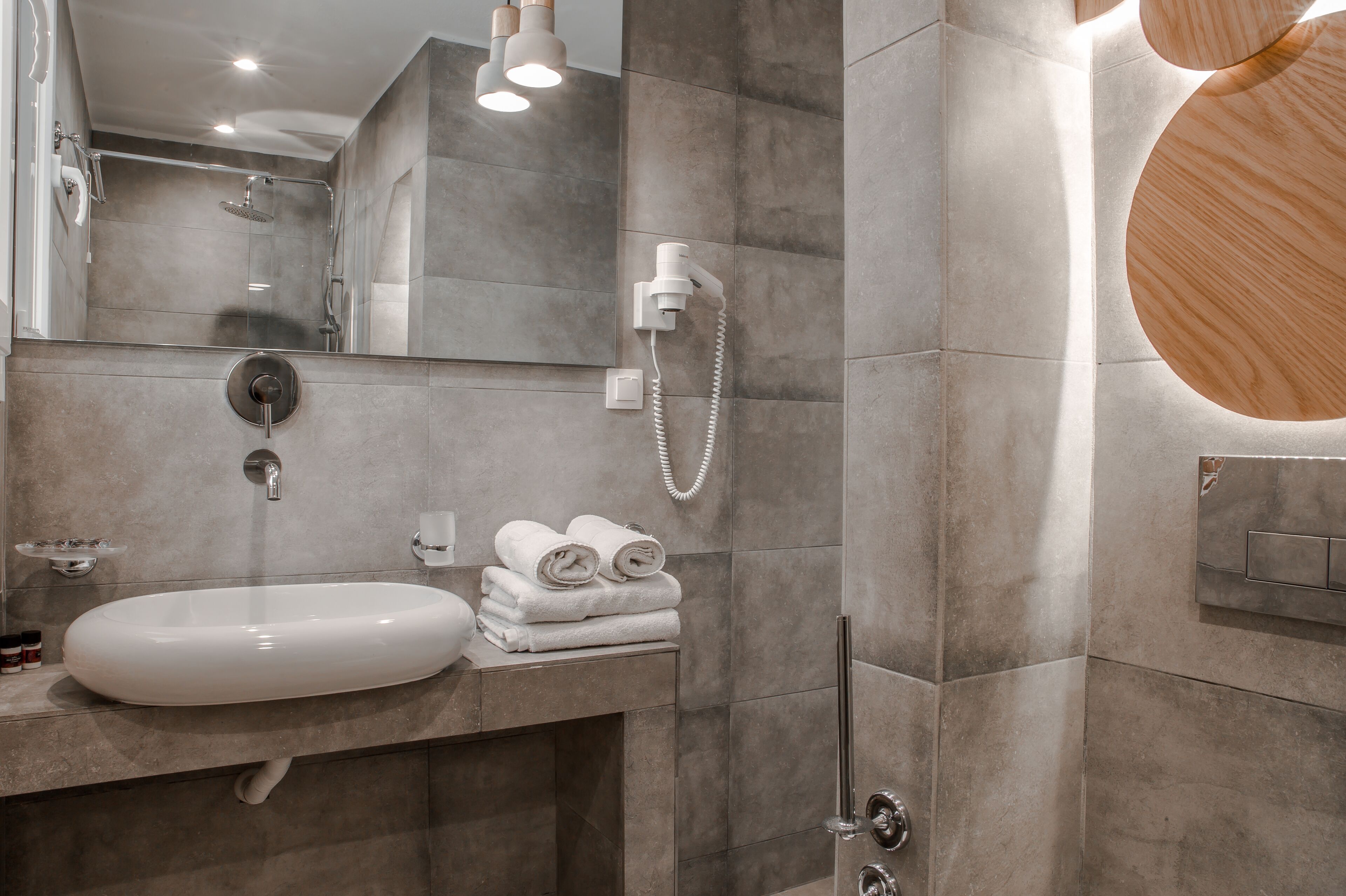 A modern bathroom with a large mirror, a sink, a shower, and a towel rack.