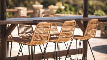A wooden table with wicker chairs, set outdoors with a blurred background of greenery.