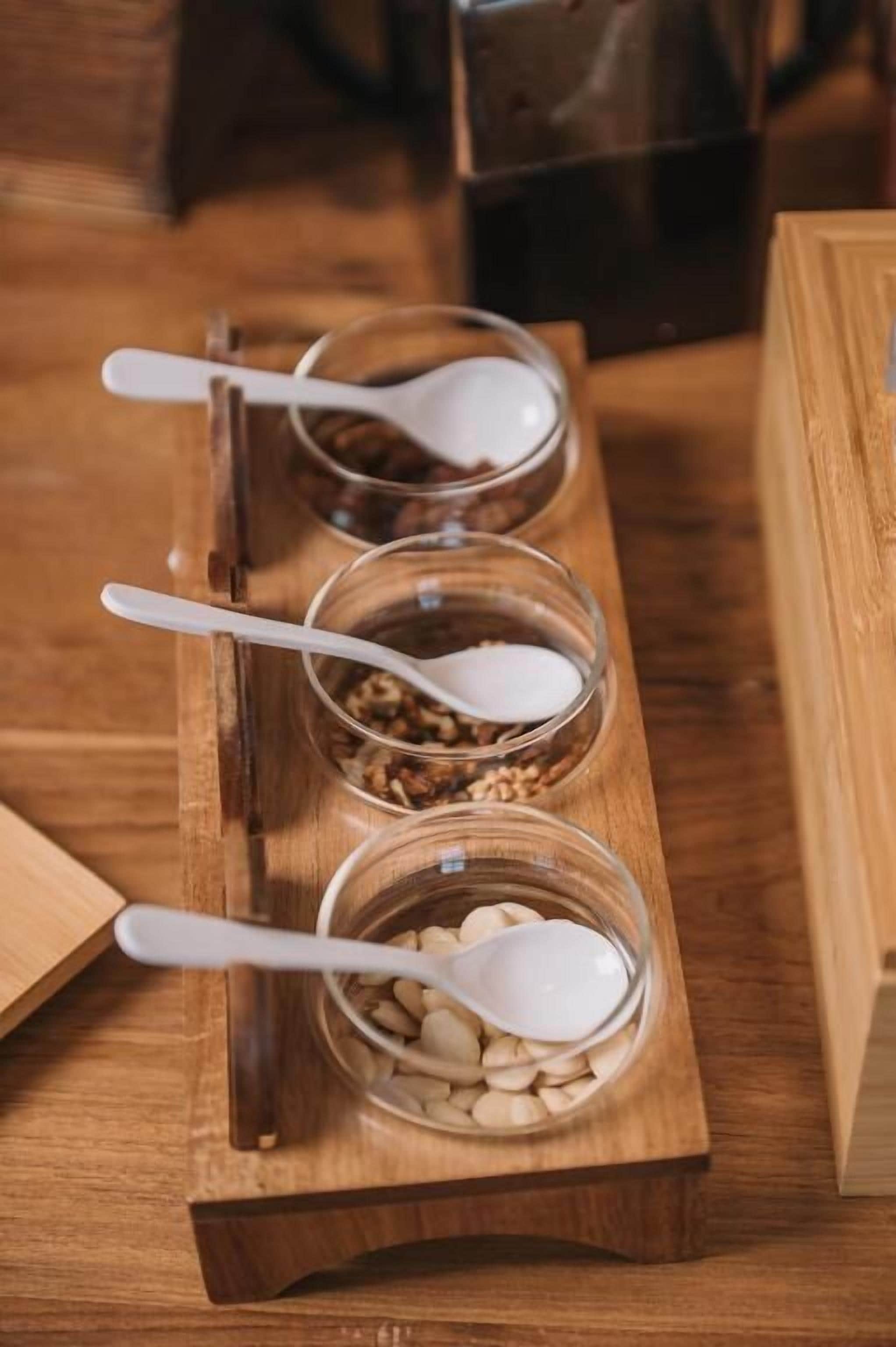A wooden tray with three glass bowls containing different food items, each with a spoon.