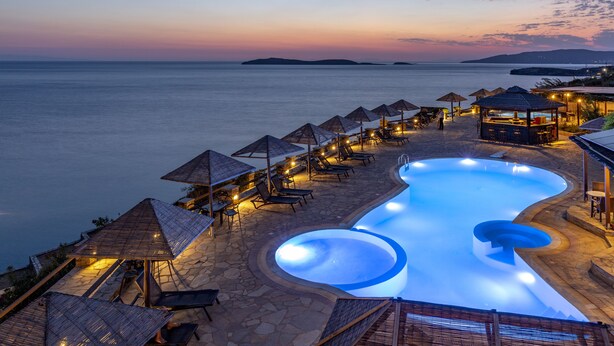 A resort pool with lounge chairs and umbrellas, surrounded by stone pathways and overlooking the sea. - Blue Bay Resort Village (Andros)