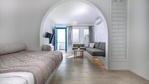 A modern room with a bed, a sofa, a small table, and a large arched doorway. - Blue Bay Resort Village (Andros)
