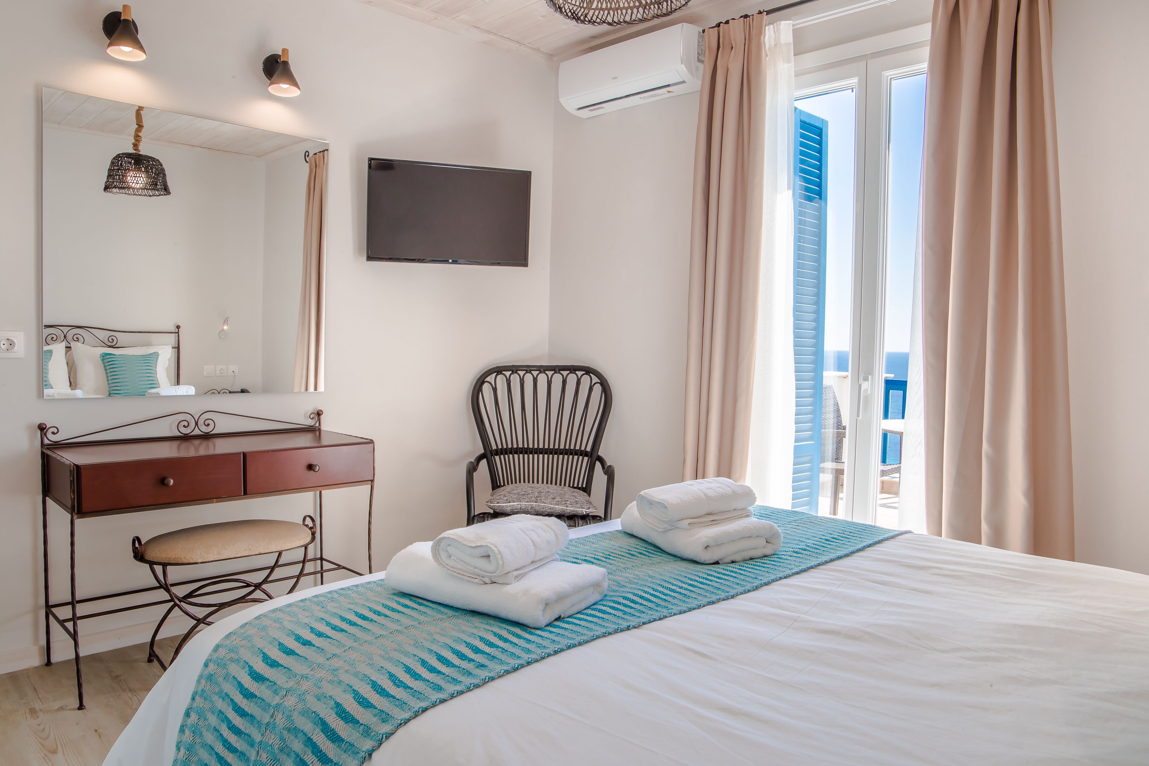 Habitación de hotel con cama, escritorio con silla, televisión y vista al mar por la ventana.