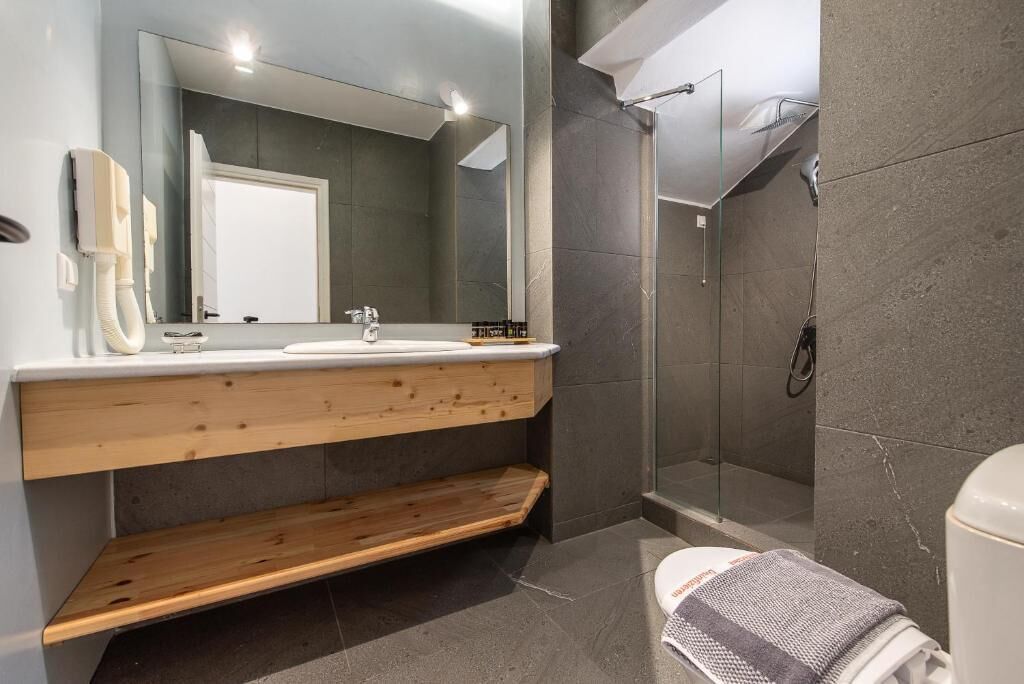 A modern bathroom with a large mirror, a wooden vanity, a shower, and a toilet.