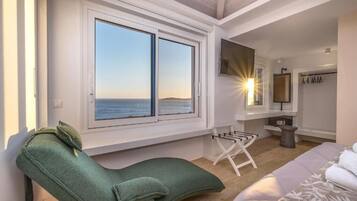 A bedroom with a large window, a green chair, a bed, and a TV.