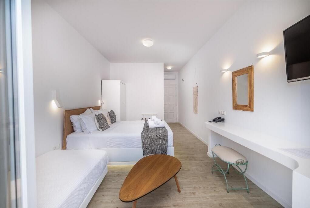 Ein Schlafzimmer mit zwei Betten, einer Holzbank, einem kleinen Hocker, einem Fernseher und einem Spiegel.