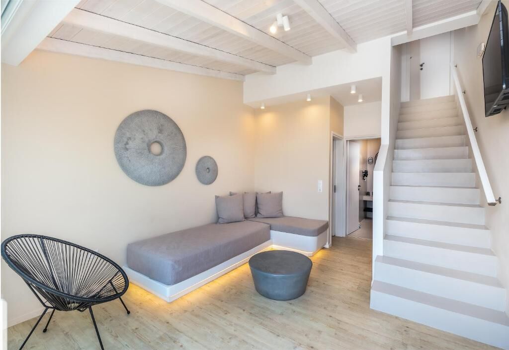 Una sala moderna con un sofá modular, una silla negra, un otoman redondos y una escalera.