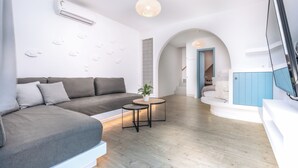 A modern living room with a grey sectional sofa, a small round table, and a flat-screen TV mounted on the wall. - Blue Bay Resort Village (Andros)