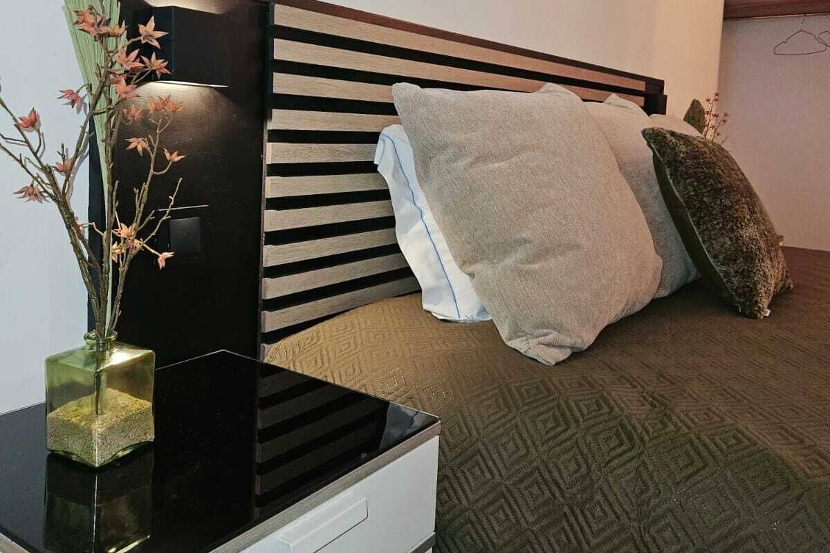 A bedroom with a bed, a bedside table with a vase of flowers, and a wall-mounted shelf.