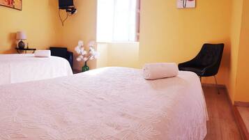 Quarto de hotel com duas camas, televisão, janela, cadeira e um vaso com flores.