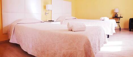 A hotel room with two beds, a small table with a lamp, and a painting on the wall.