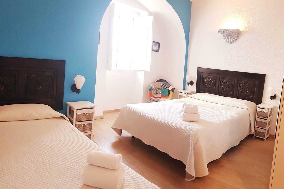 A hotel room with two beds, a wooden floor, and a blue accent wall.