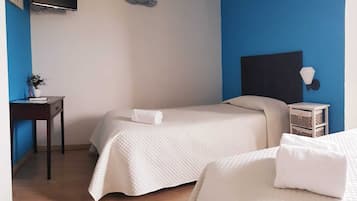 A hotel room with two beds, a desk, a TV, and a wall-mounted light fixture.
