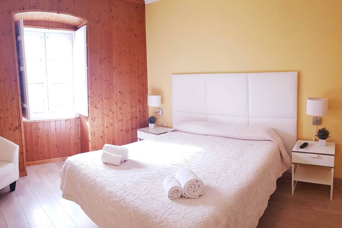 A hotel room with a large bed, wooden walls, a window, and a bedside table with a lamp.