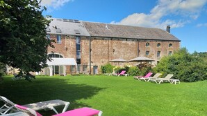 Un bâtiment à l’extérieur en briques, une pelouse avec des chaises longues et des parasols.