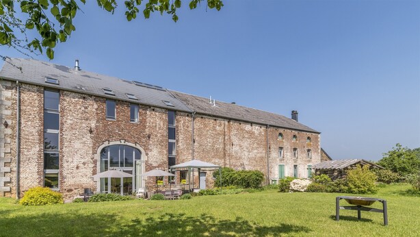 Un grand bâtiment en briques, doté d’un toit plat, d’un patio couvert avec des sièges extérieurs et d’une pelouse bien entretenue.