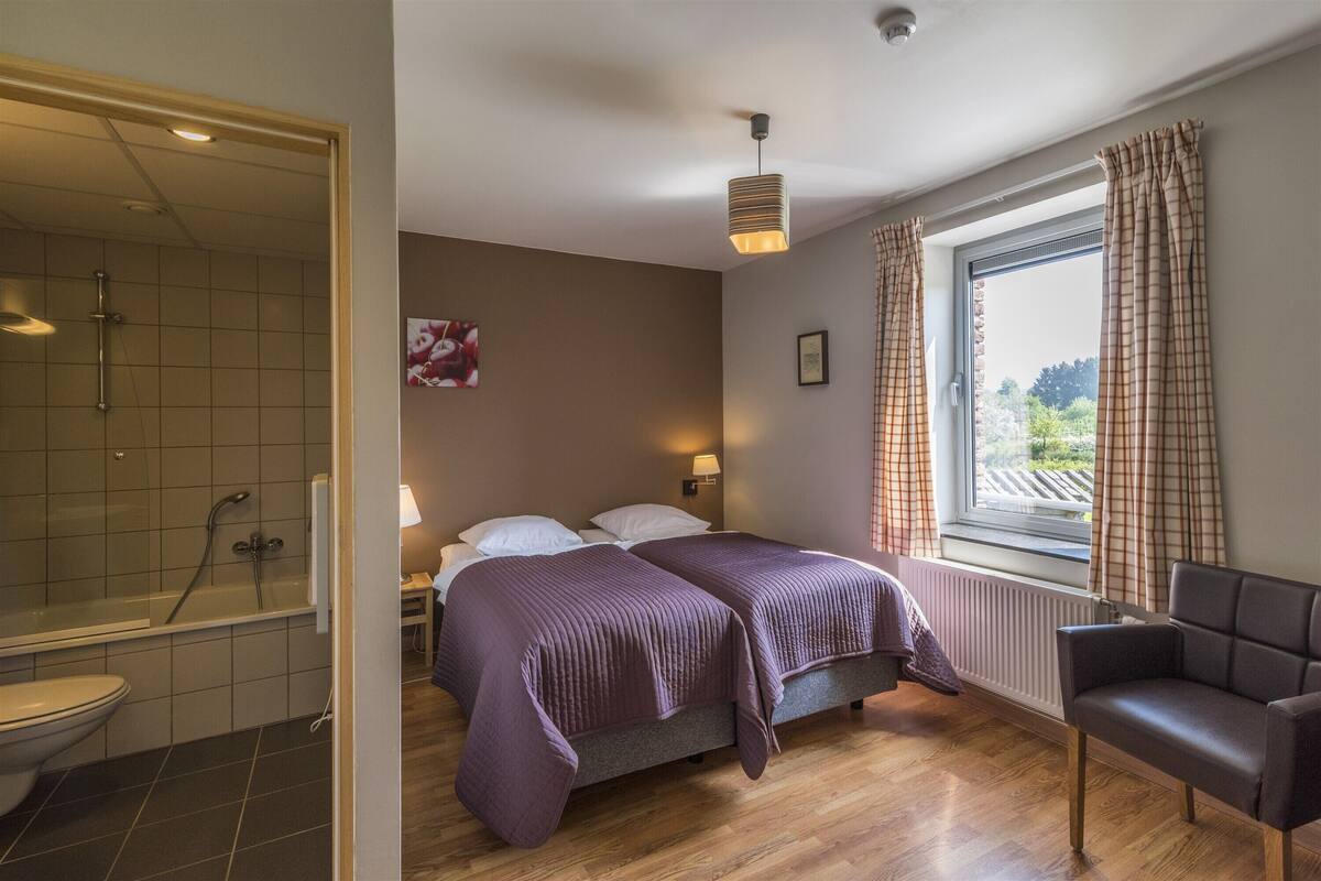 Ein Schlafzimmer mit Bett, Stuhl, einem Vorhangfenster, einer Dusche und einer Wandleuchte.