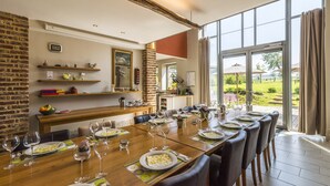 Un espace repas avec une longue table dressée pour le repas, un mur en briques et une vue sur l’extérieur.