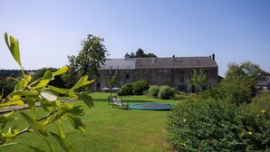 Un grand bâtiment en pierre, doté d’une pelouse bien entretenue, d’une petite piscine et entouré de verdure.