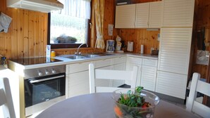 A compact kitchen with wooden walls, a built-in oven, a sink, and white cabinets. - Wilgenhof (Hotton)