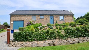 A two-story stone building with a blue door and windows, surrounded by well-maintained gardens and a stone pathway. - Wilgenhof (Hotton)