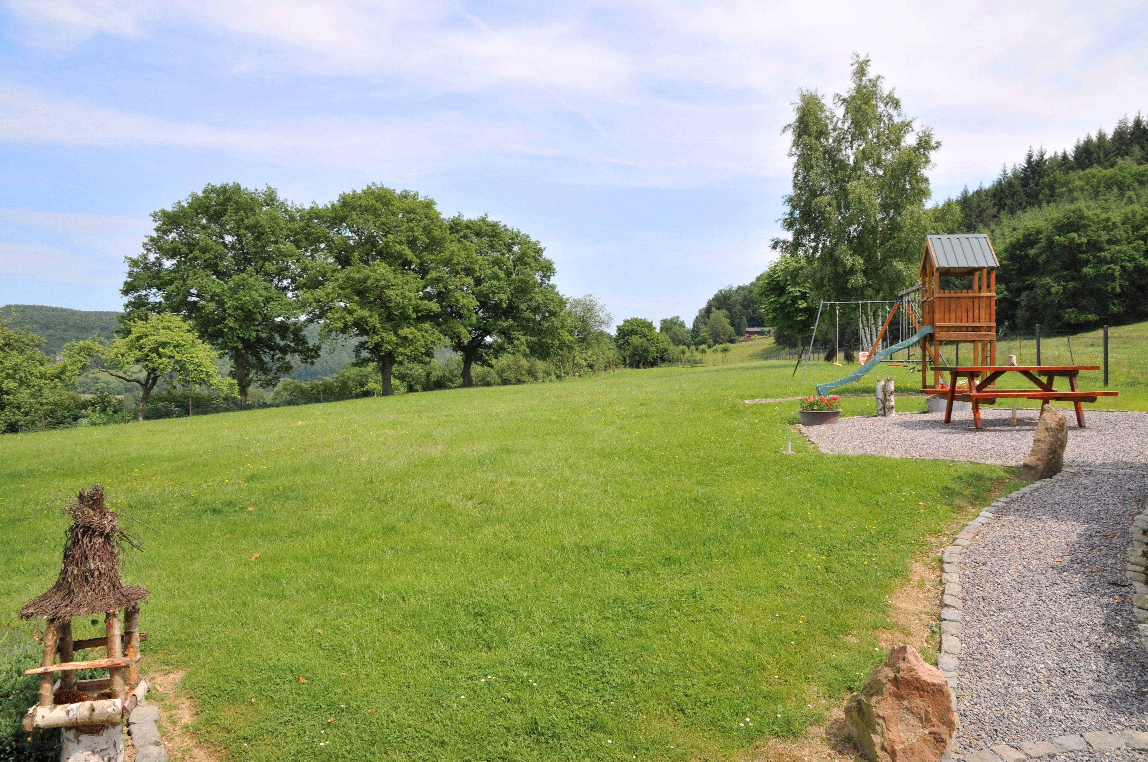A playground with a slide and climbing structures in a grassy field with trees in the background.