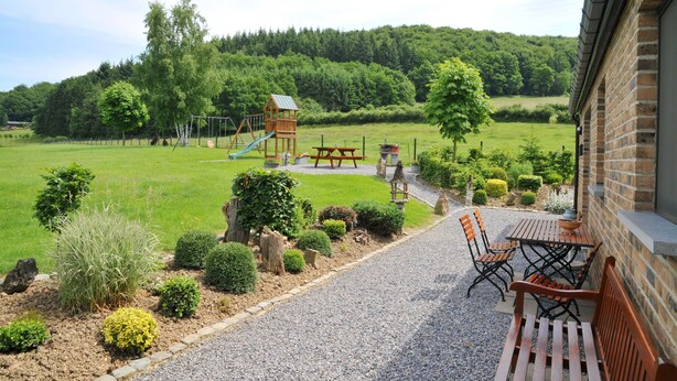 A patio with a table and chairs, a playground with a slide, and a garden with various plants. - Wilgenhof (Hotton)