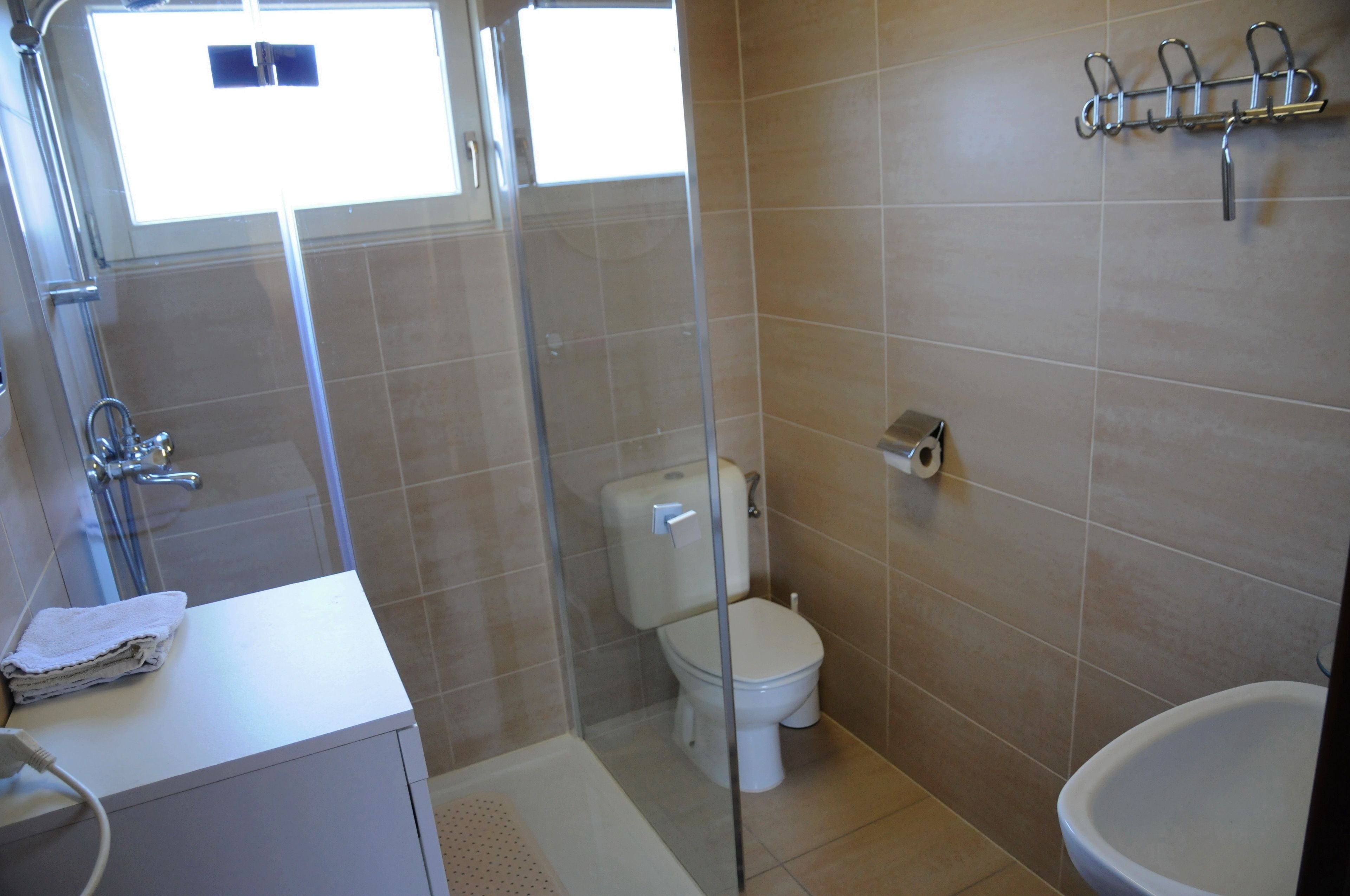 A bathroom with a glass-enclosed shower, a toilet, and a sink with a towel.
