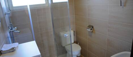 A bathroom with a glass-enclosed shower, a toilet, and a sink with a towel.