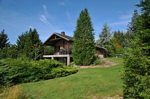 A cabin with a deck, surrounded by dense forest and a well-maintained lawn. - Le Pre Vert (Durbuy)