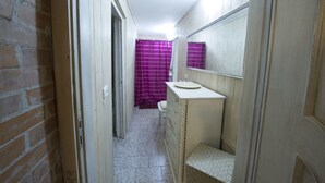 A narrow hallway leading to a bathroom with a purple shower curtain, a sink, and a mirror. - La cutizza (Martina Franca)