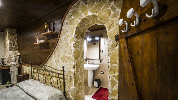 A rustic bedroom with a stone archway leading to a bathroom, featuring a wooden bed, a stone fireplace, and a red rug. - La cutizza (Martina Franca)