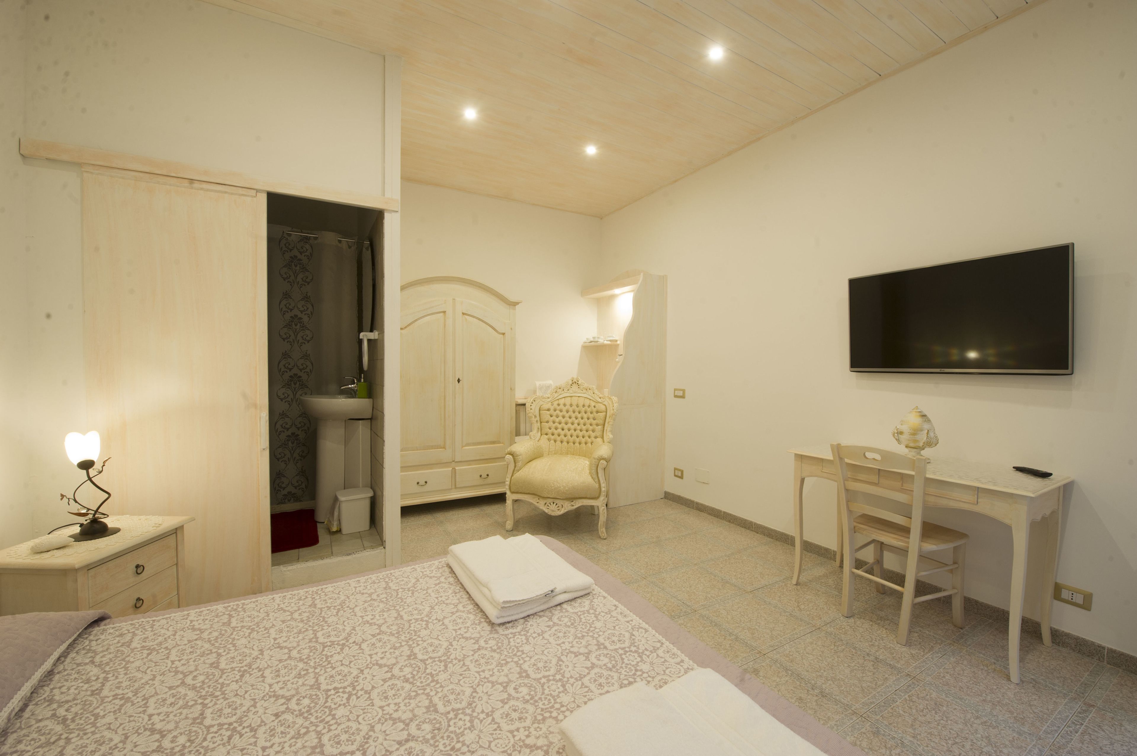 A bedroom with a bed, bedside table, wardrobe, desk, chair, and a TV mounted on the wall.