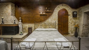 A bedroom with a stone wall, wooden ceiling, a bed with a metal frame, a dresser, a statue, and a clock on the wall. - La cutizza (Martina Franca)