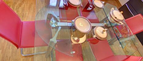 A round glass table with six red chairs, surrounded by a wooden floor.