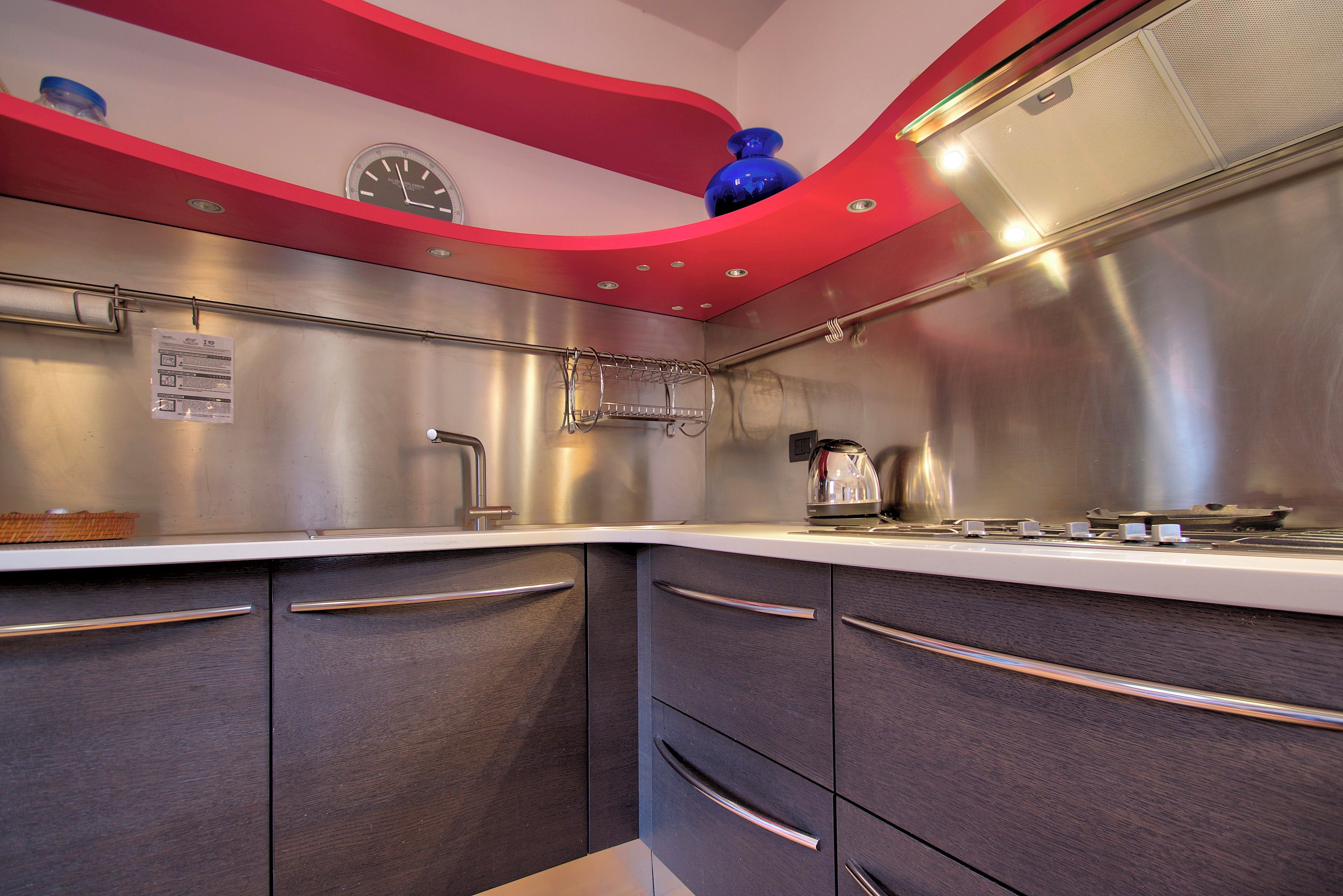 A modern kitchen with stainless steel appliances, a clock, and a red accent wall.