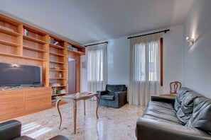 Una sala de estar con televisor, estantería de madera, sofá de cuero y una mesita.