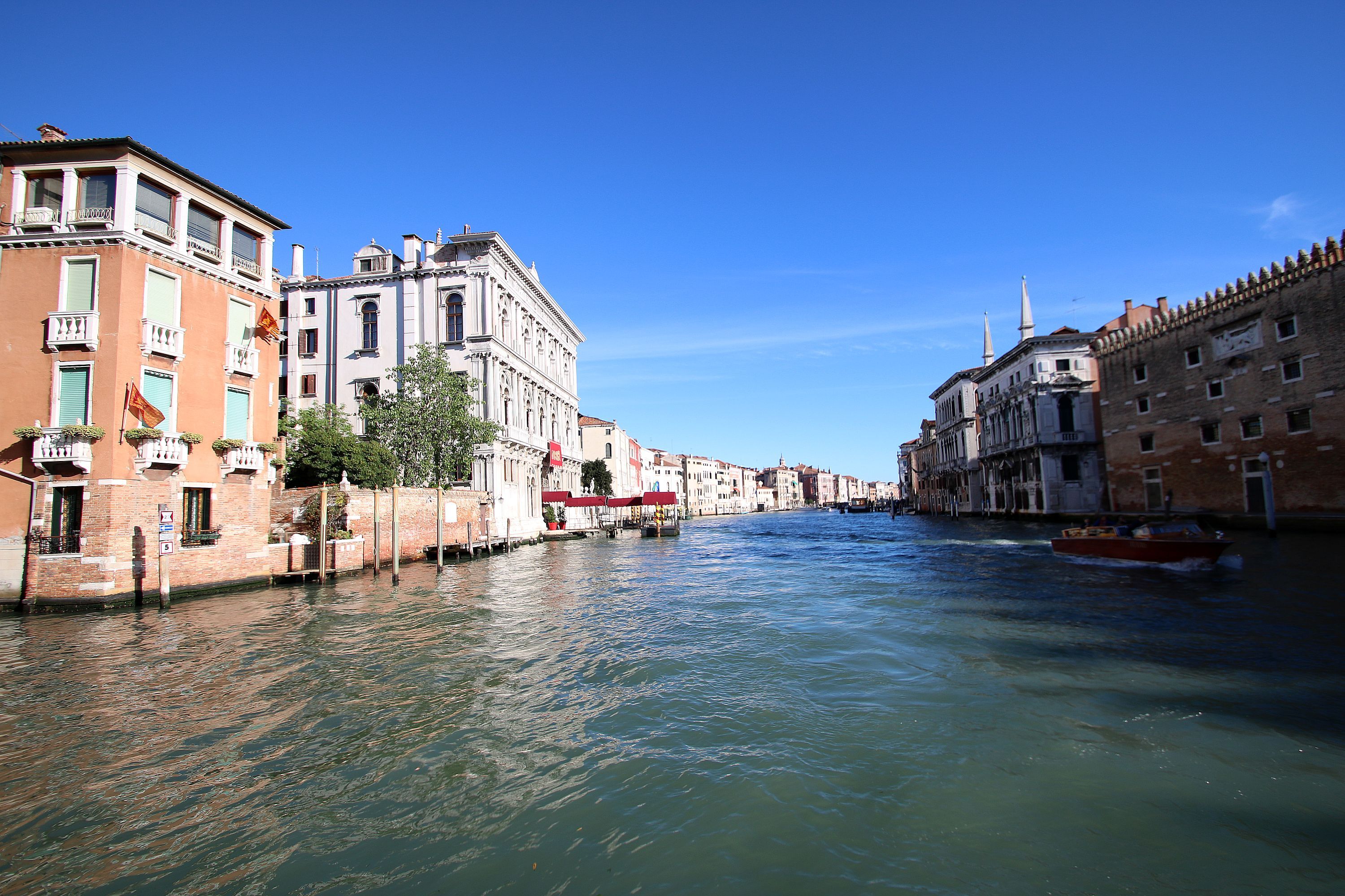 A canal with buildings on either side, a boat in the water, and a clear blue sky.