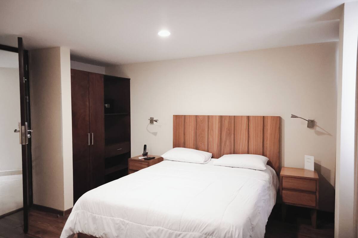 A hotel room with a large bed, wooden headboard, bedside tables, and a wardrobe.