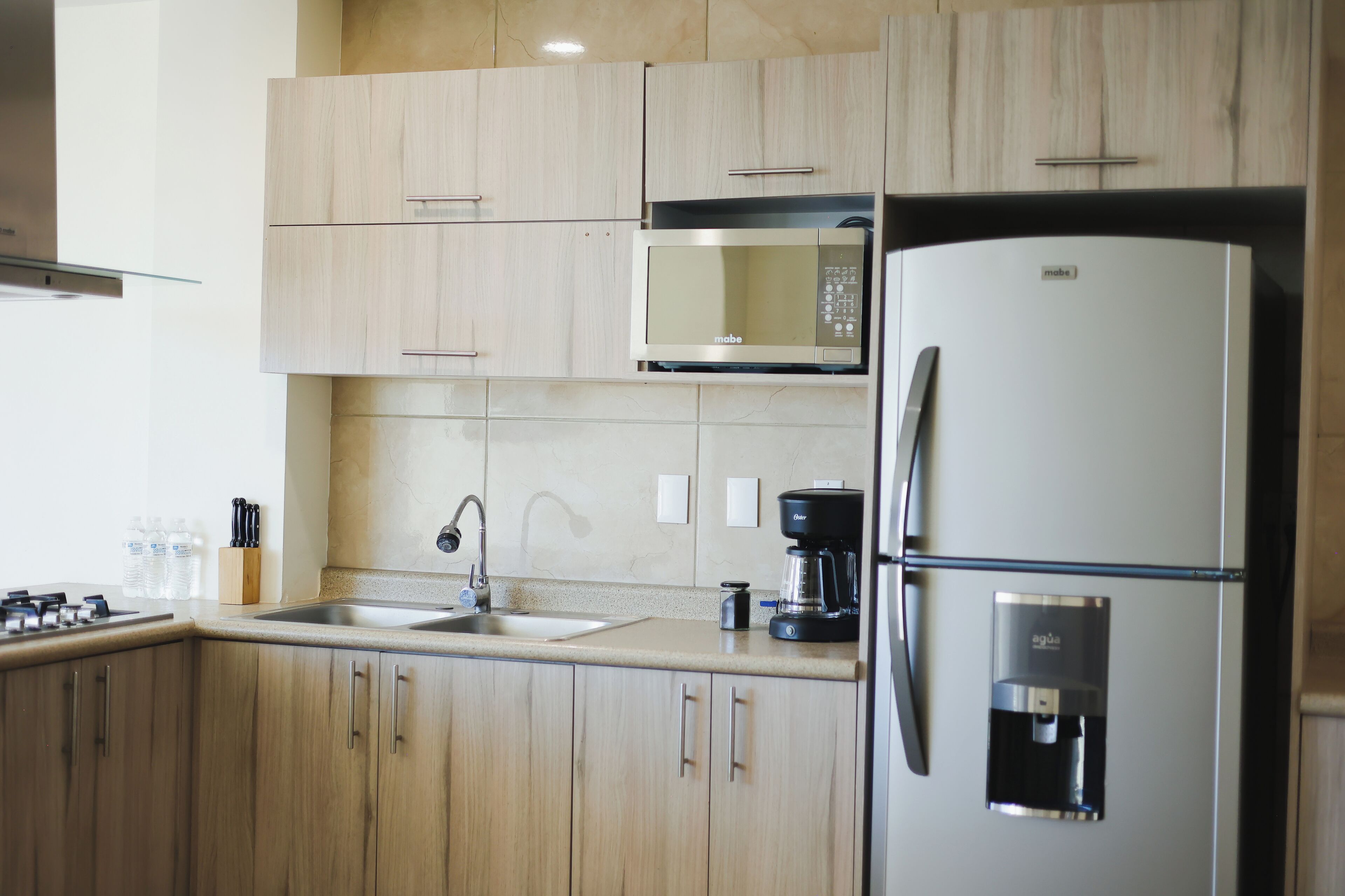 Una cucina moderna con mobili in legno, un frigorifero in acciaio inossidabile, un forno a microonde integrato, una macchina da caffè e un dispenser per l'acqua.