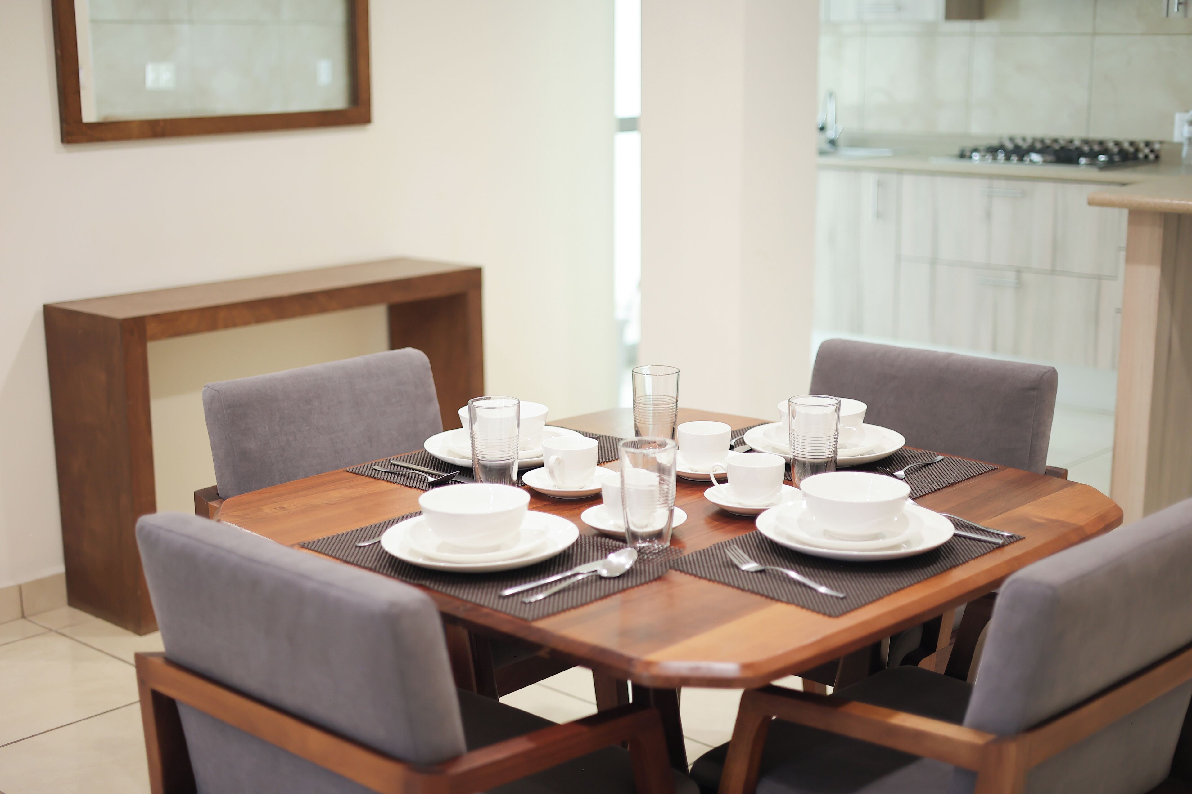 A dining table set with white plates, bowls, and glasses, surrounded by grey upholstered chairs.