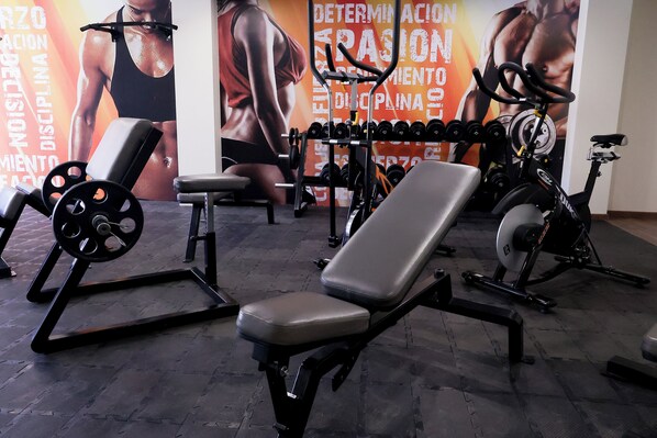Una palestra con attrezzature per sollevamento pesi, una panca e una cyclette.