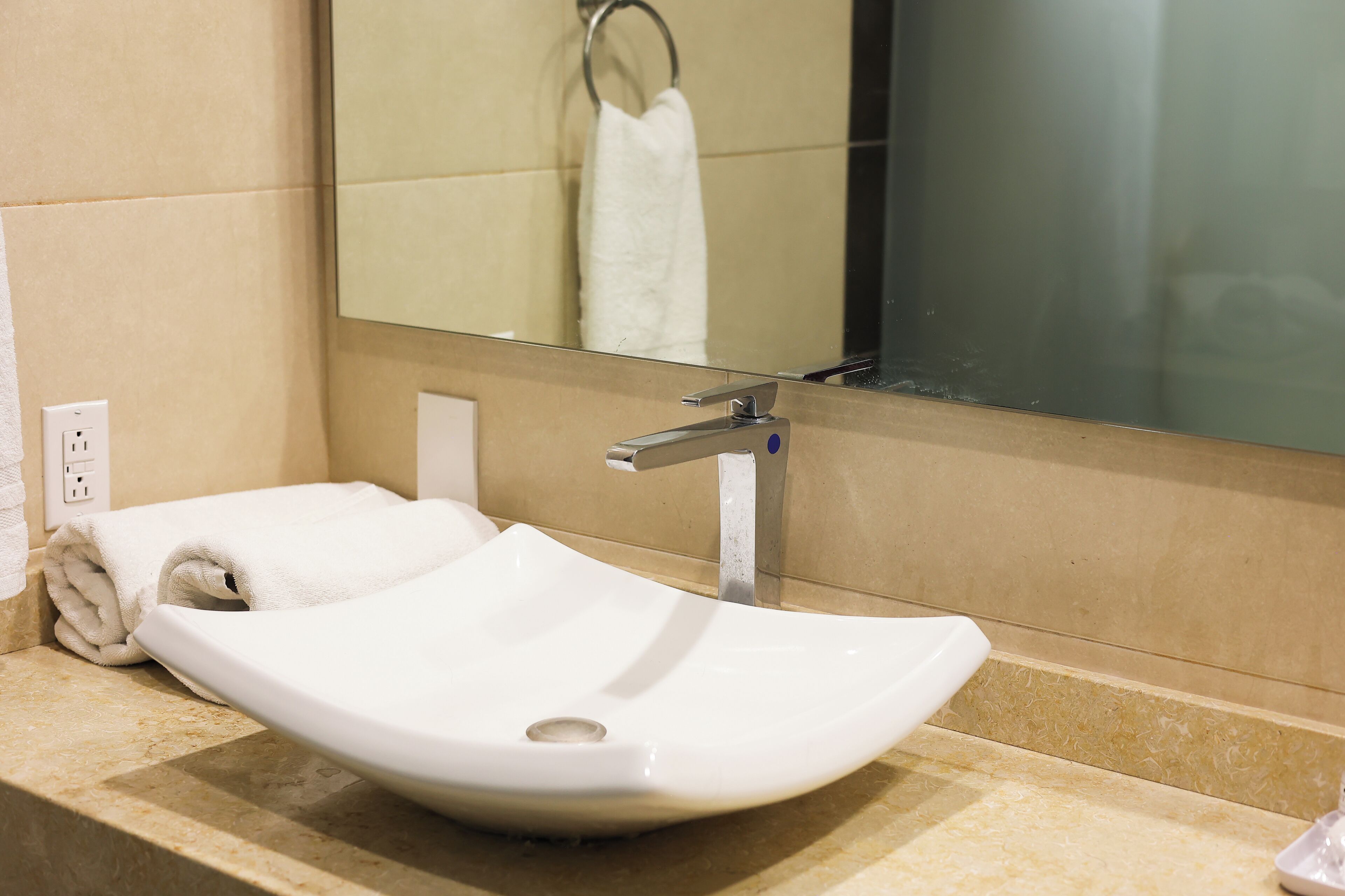 A white vessel sink with a single faucet, a towel, and a mirror in a bathroom.