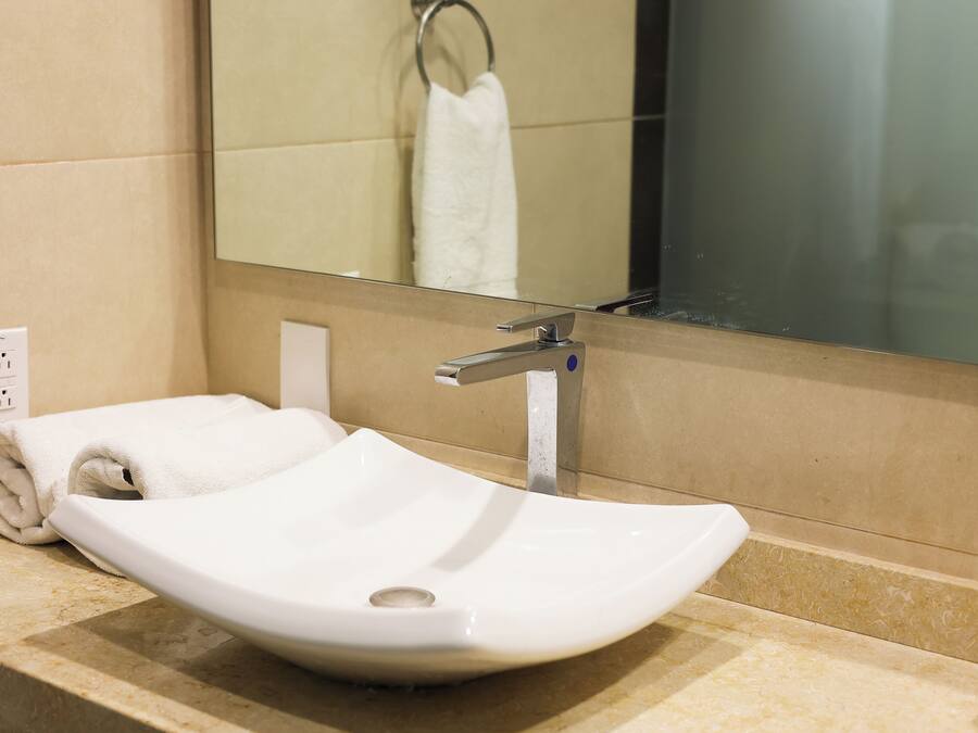 A white vessel sink with a single faucet, a towel, and a mirror in a bathroom.