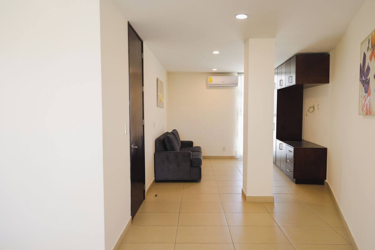 A hallway with a dark-colored sofa, a small kitchenette, and a door on the left.
