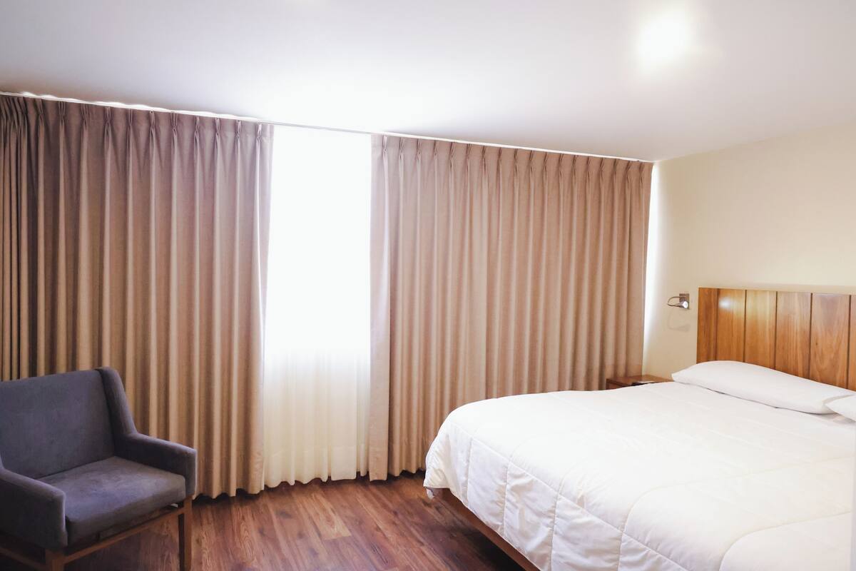 A hotel room with a bed, a chair, and curtains.