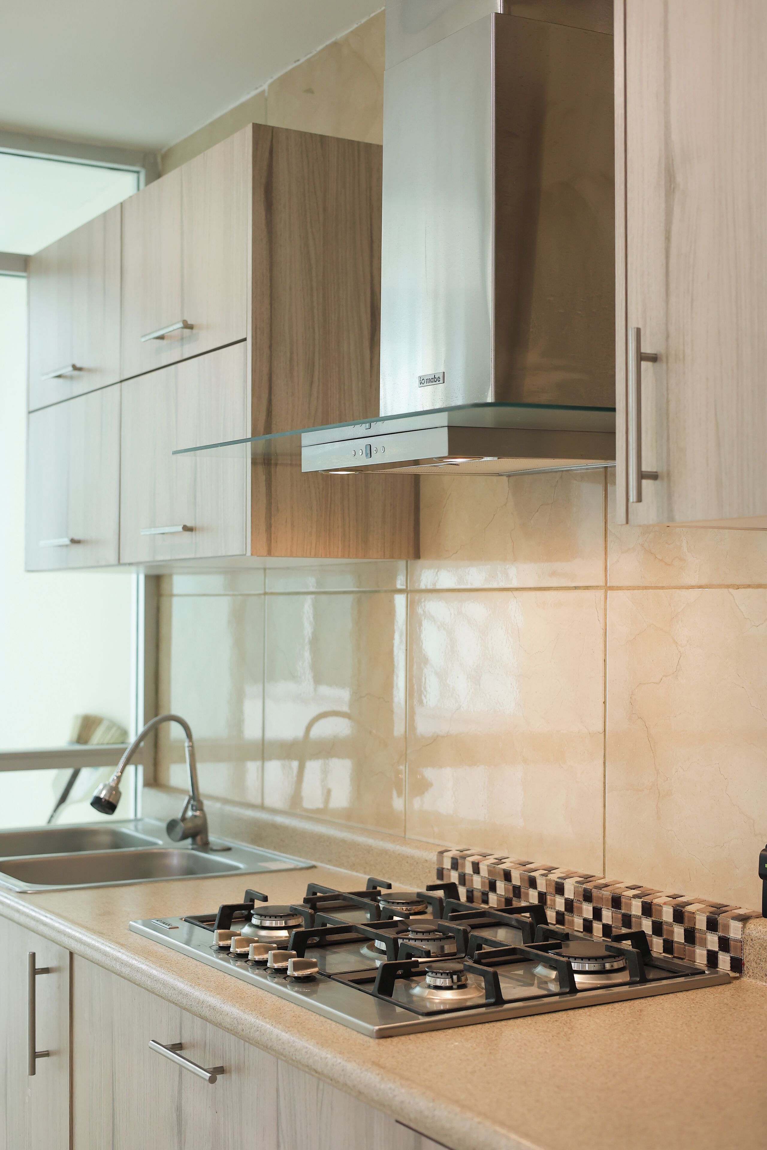 A modern kitchen with light wood cabinets, a stainless steel range hood, and a gas stove.