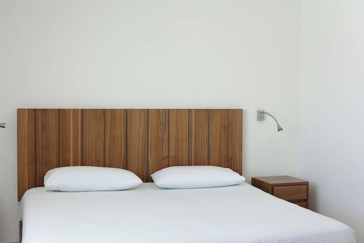 A bed with a wooden headboard, two white pillows, and a bedside table with a lamp.