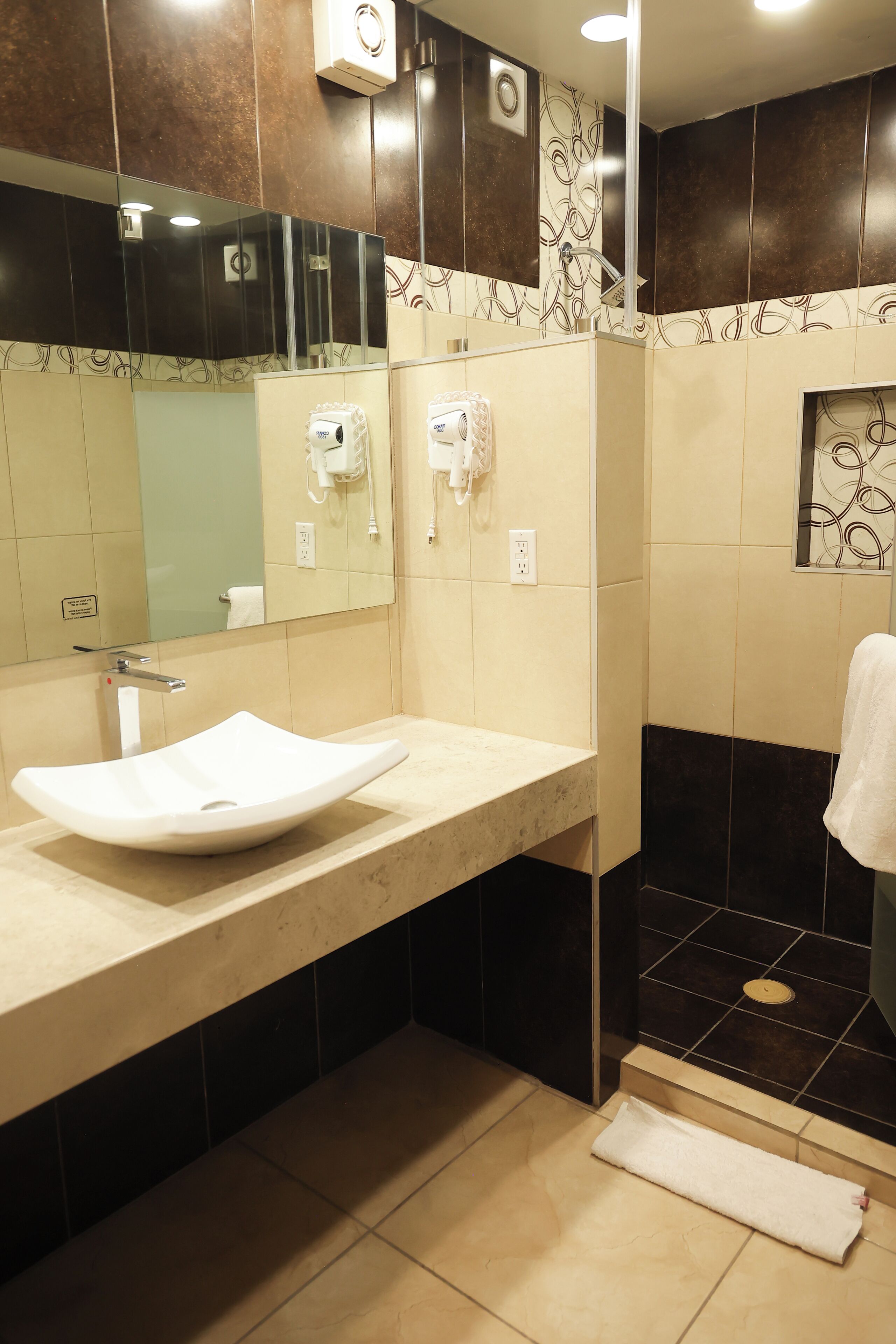 A modern bathroom with a large sink, a mirror, a towel rack, and a shower area.